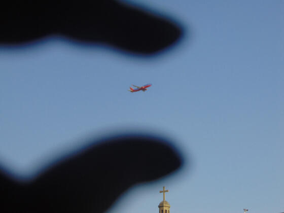 Perspective of airplane between fingers above a church