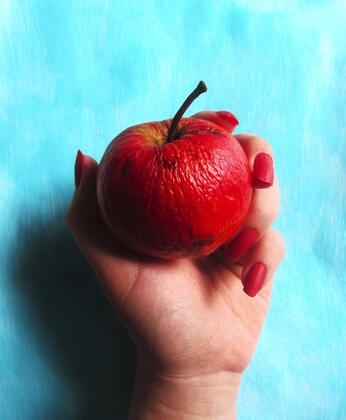 Hand with red nails holding apple with turqoise background