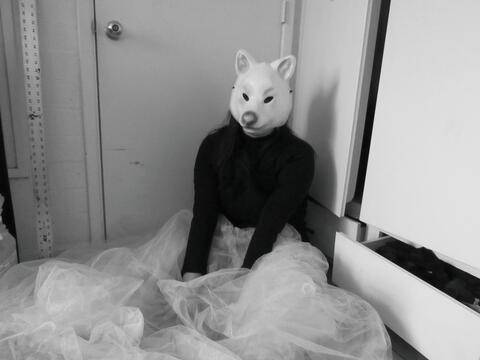 Black and White photo of masked girl with a large tool skirt sitting in front of a door