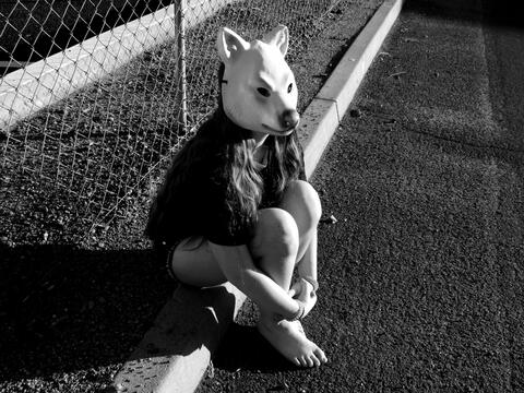 Black and White photo of girl with wolf masked sitting on curb